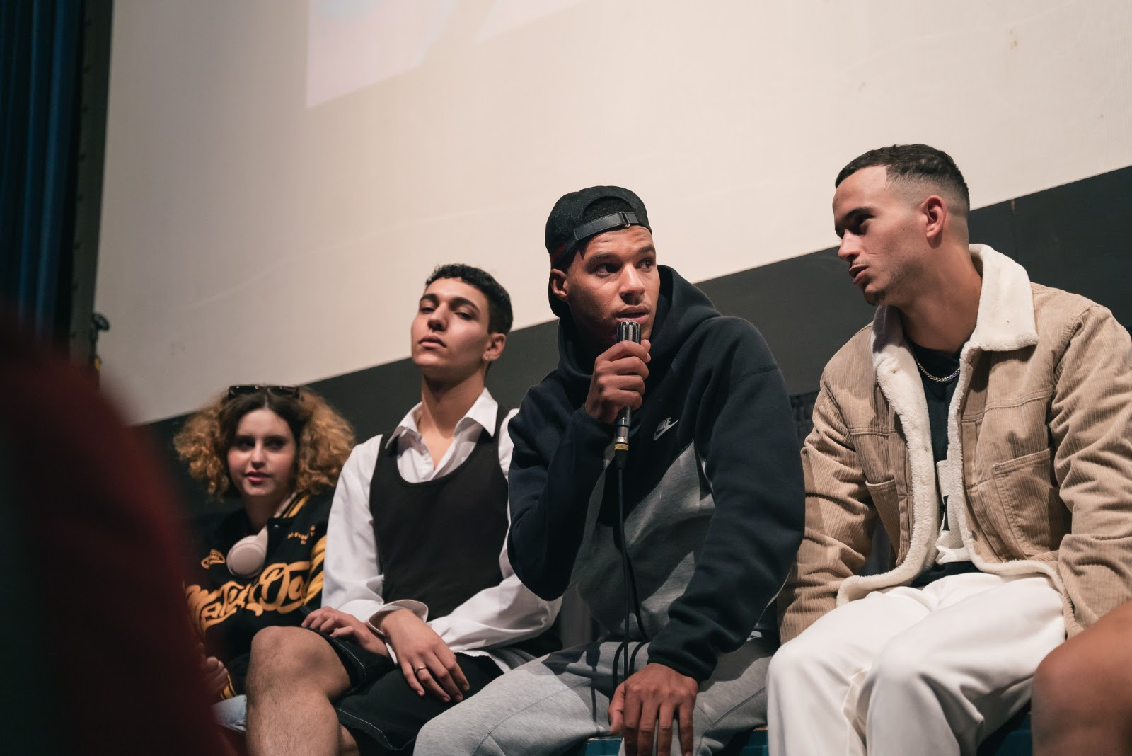 Joves migrats parlen asseguts a l'escenari del teatre comtal de Ripoll amb joves del Ripollès 