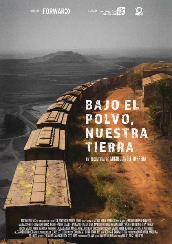 Pòster del documental 'Bajo el polvo, nuestra tierra'. Mostra una vista aèria d'un tren que passa per una zona desèrtica, amb unes muntanyes al fons. El tren sembla estar carregat de carbó i passa per un paisatge que ha estat afectat per la mineria. El títol del documental es troba a la part central de la imatge i els crèdits a la part superior i inferior.
